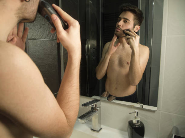 portrait of handsome caucasian man reflection in from of the mirror, shaving with a shaver - shaving men electric razor reflection imagens e fotografias de stock