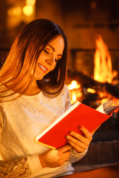 istock Woman reading book at fireplace. Winter home relax 1204256963
