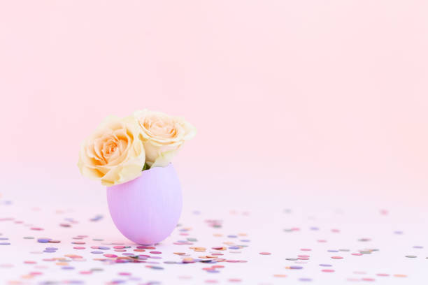Purple easter eggshell with yellow,orange,beige pastel small roses on pink background, multicolor confetti. Egg is symbol of celebration of a religious holiday among Catholics, Christians,Protestants.