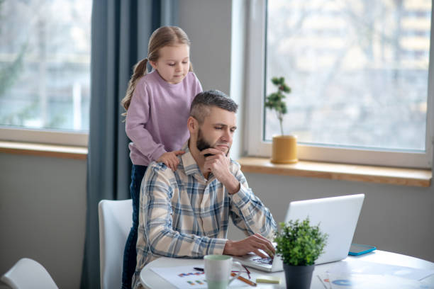 istock Seated focused dad, daughter standing behind, they are looking into laptop. 1204258625