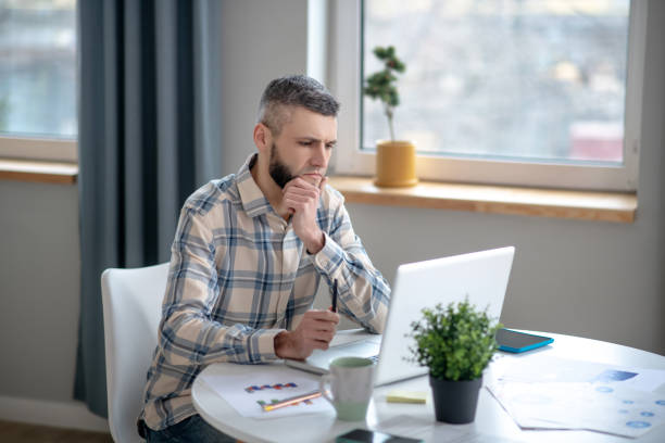 istock Young man in a plaid shirt sitting looking at a laptop. 1204258633