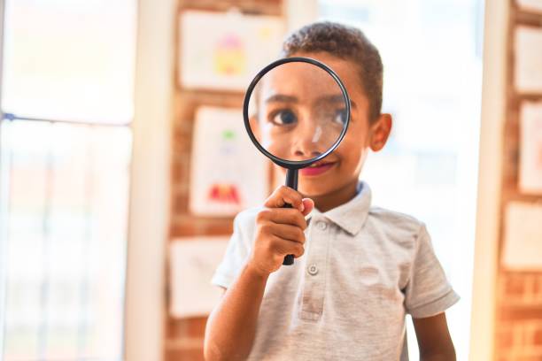 hermoso niño afroamericano jugando con la loupe en el jardín de infantes - curiosity searching discovery home interior fotografías e imágenes de stock