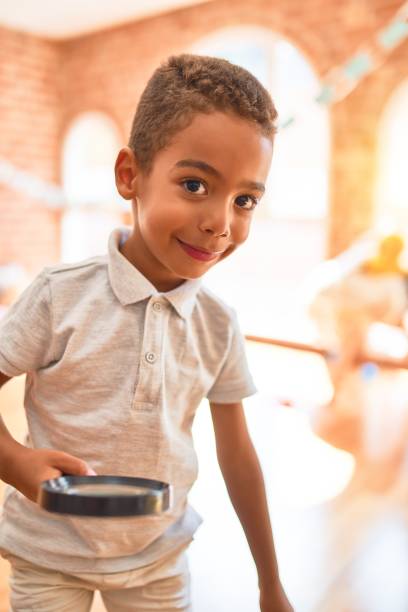 hermoso niño afroamericano jugando con la loupe en el jardín de infantes - curiosity searching discovery home interior fotograf�ías e imágenes de stock