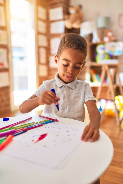 istock Beautiful african american toddler drawing using paper and marker pen at kindergarten 1204259727