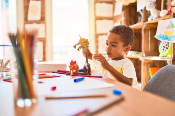 Beautiful african american toddler playing with dinosaurs toy on desk at kindergarten Beautiful african american toddler playing with dinosaurs toy on desk at kindergarten jurassic photos stock pictures, royalty-free photos & images