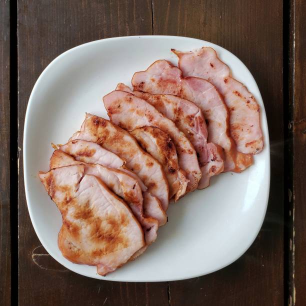 Canadian Back Bacon, pan fried and sliced slices of Canadian back bacon in a pile on a white plate cooked bacon slice stock pictures, royalty-free photos & images