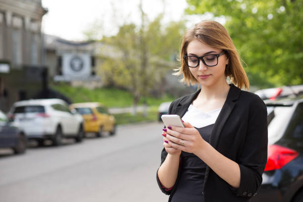 woman texting while waiting for taxi bus. half length body woman girl looking at cell phone mobile interest smile on face outdoors city urban cars on background - half smile imagens e fotografias de stock