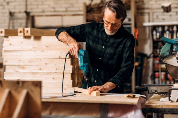 istock Carpenter using electric drill. Senior man making a hole in a wooden board. 1204267615