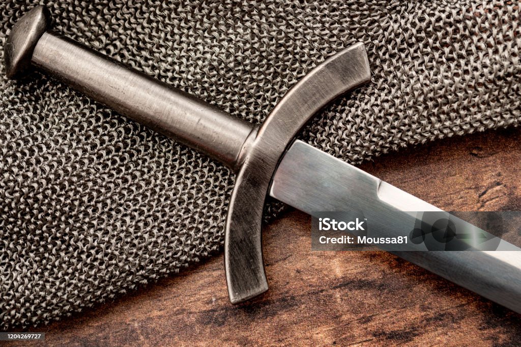 Medieval weapons and middle ages warfare conceptual idea with close up on sword on steel chain mail or maille on wooden background Sword Stock Photo