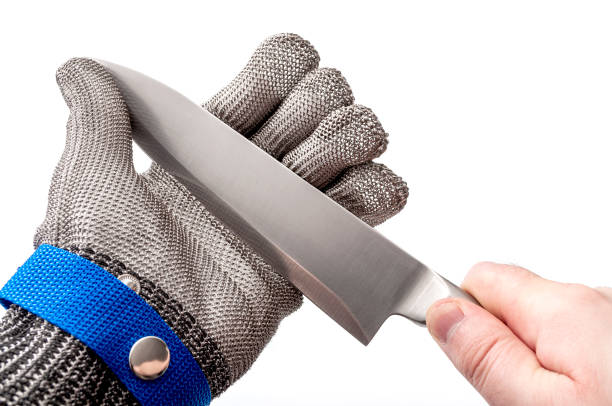 Work safety and protective gear for safe working environment conceptual idea with hand wearing metal mesh protection glove and holding stainless steel knife by the blade isolated on white background Work safety and protective gear for safe working environment conceptual idea with hand wearing metal mesh protection glove and holding stainless steel knife by the blade isolated on white background knife crime photos stock pictures, royalty-free photos & images