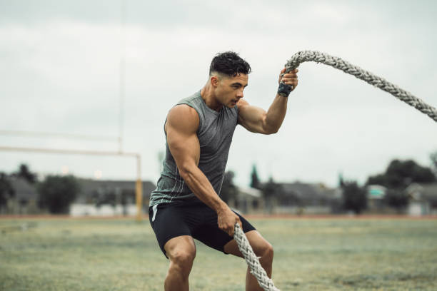 Strong man exercising with battle ropes on a field Strong man exercising with battle ropes. Athlete doing battle rope workout outdoors on a field. cross training photos stock pictures, royalty-free photos & images