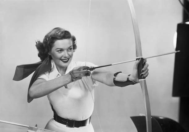 Young woman aiming arrow, smiling  bow and arrow photos stock pictures, royalty-free photos & images