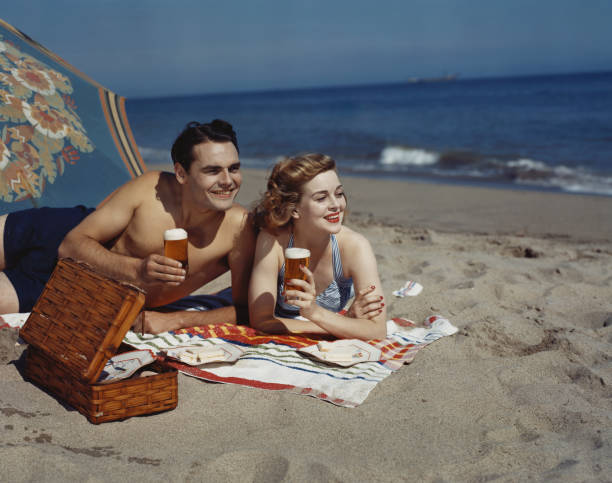 junge pärchen am strand mit bier, lächeln - archival stock-fotos und bilder