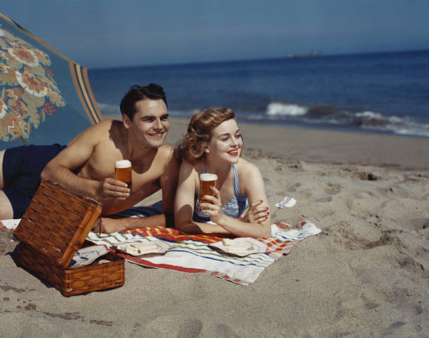 Young couple lying on beach with beer, smiling  swimwear photos stock pictures, royalty-free photos & images