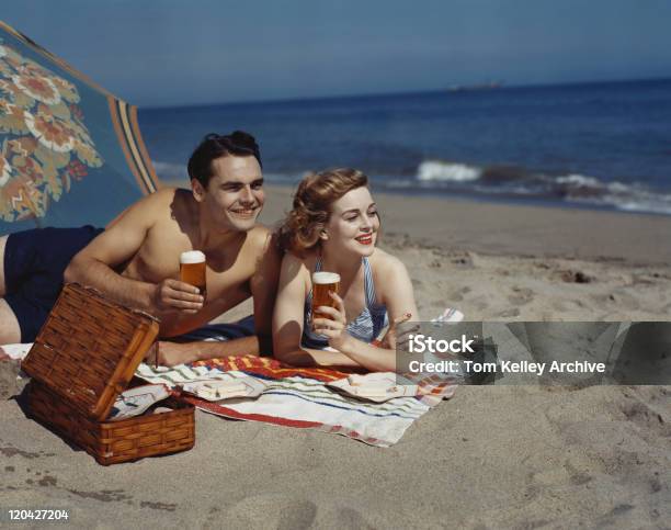 Young Couple Lying On Beach With Beer Smiling Stock Photo - Download Image Now - Archival, Beach, Beer - Alcohol