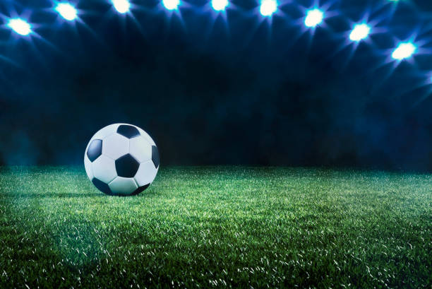 Football or soccer ball background with spotlights Football or soccer background with a row of spotlights illuminating a ball on the green turf in a stadium in a sports championship or World Cup event in a panorama banner stadium playing field grass fifa world cup stock pictures, royalty-free photos & images