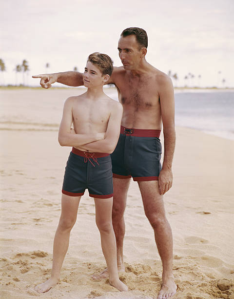 vater und sohn stehen am strand, vater zeigt - swimming trunks fotos stock-fotos und bilder