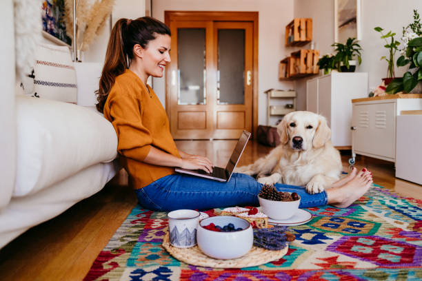 junge frau arbeitet auf laptop zu hause. niedlichen goldenen retriever hund neben. gesunde frühstückszeit. technologie und lifestyle in innenräumen - people business dog owner stock-fotos und bilder