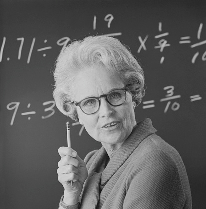 Close-up on female student or teacher in horn rimmed glasses standing against green chalkboard. She is tired of learning, teaching, school and exams. Retro style. Heavy processing for retro look, slight vignette added.