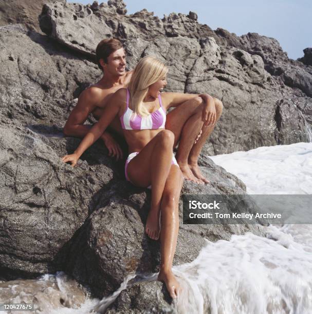 Young Couple Sitting On Rocks Stock Photo - Download Image Now - 1968, Archival, Beach