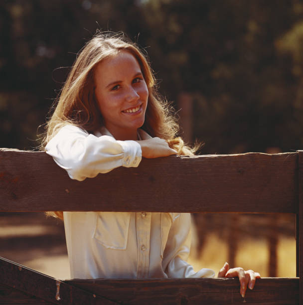 Young woman leaning on fence, smiling, portrait  1970s woman stock pictures, royalty-free photos & images