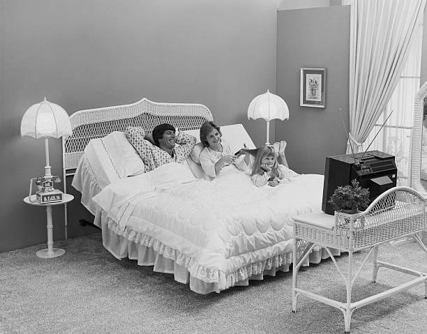Father and mother with daughter lying on bed watching tv, smiling  1974 stock pictures, royalty-free photos & images