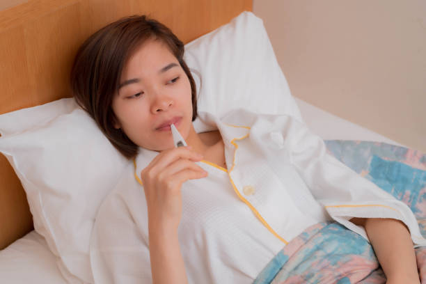 istock a young woman in bed using a thermometer 1204279371