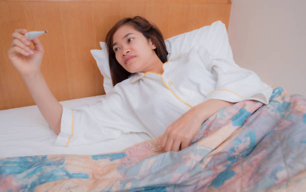 istock a young woman in bed using a thermometer 1204279378