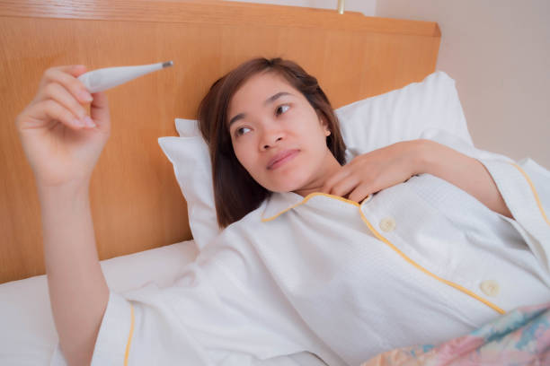 istock a young woman in bed using a thermometer 1204279441