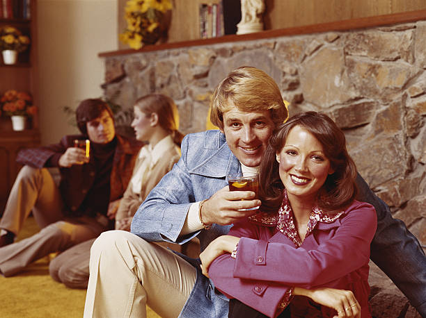 Couples sitting by fireplace having drinks, smiling  1970s woman stock pictures, royalty-free photos & images