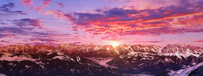 Aerial panorama of tourist resort with lake, Alp mountain summits and skiing slopes under dramatic sunset sky