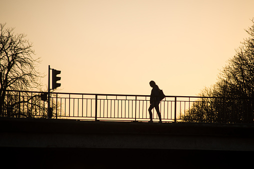 view of silhouette of woman walking on the bridge by sunset