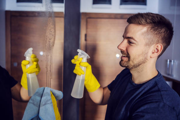 Side view of attractive man with rubber gloves on standing in front of mirror on wardrobe, spraying and cleaning it with magic cloth. Side view of attractive man with rubber gloves on standing in front of mirror on wardrobe, spraying and cleaning it with magic cloth. laundry husband housework men stock pictures, royalty-free photos & images