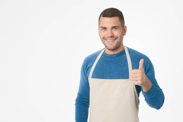 istock Young handsome shopkeeper man wearing apron doing thumb up gesture standing over isolated white background 1204283261