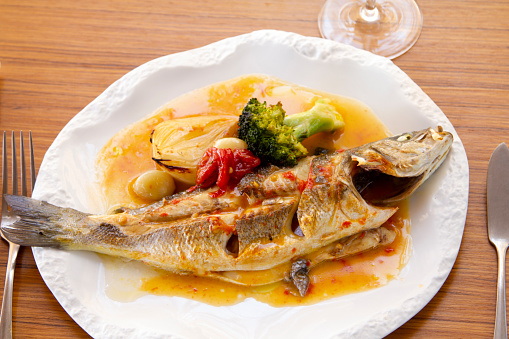 A close-up of fish baked with fresh vegetables and olive oil.