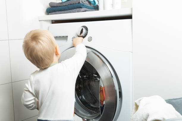 istock Two year old child doing household chores. Loading washing machine. 1204285528