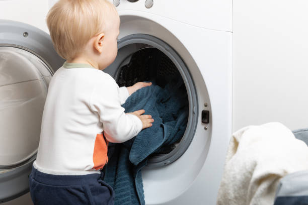 istock Two year old child doing household chores. Loading washing machine. 1204285540