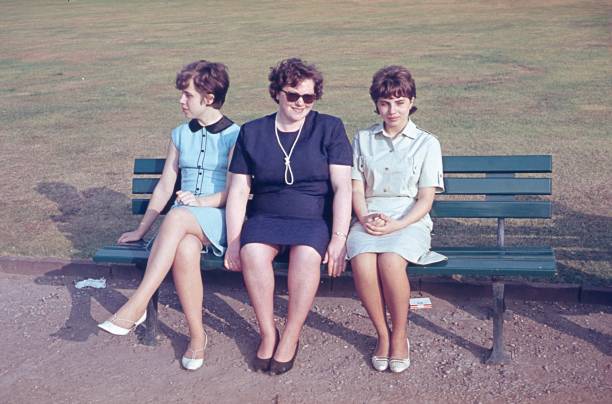 Wuppertal, North Rhine-Westphalia, Germany, 1969. A mother with her two daughters enjoy the spring sun on a park bench.