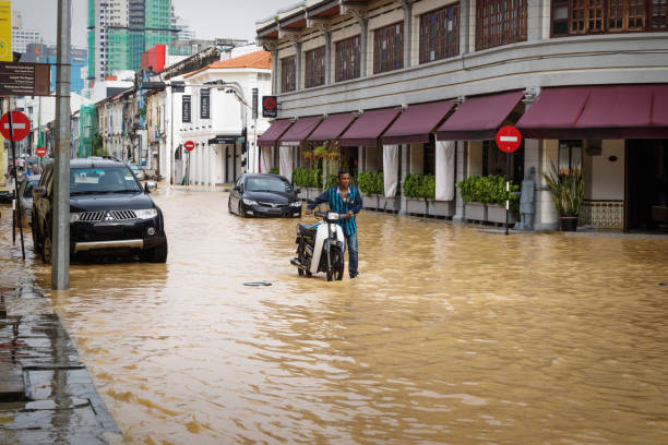 anwohner schiebt motorrad durch überflutete straße nach heftigen regenfällen in georgetown, penang, malaysia - southeast asia fotos stock-fotos und bilder