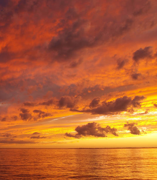 A sunny inspirational orange coloured stratocumulus cloudy coastal sunset seascape over the ocean with water reflections. Queensland, Australia.