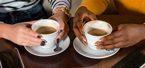 twee multi etnische meisjesvrienden die van koffie samen in een koffiewinkel genieten. close-up van handen die koffiekoppen houden.. - andrej stockfoto's en -beelden