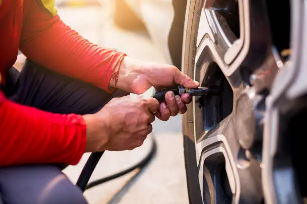 Photo of Driver checking air pressure and filling air in the tires close up, safety before trave.