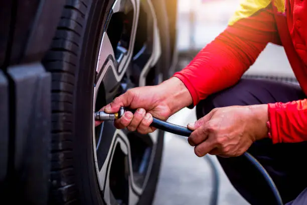 Photo of Driver checking air pressure and filling air in the tires close up, safety before trave.