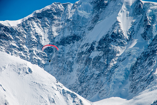 Distant paraglider flying over glaciers and snow capped iconic Swiss mountains