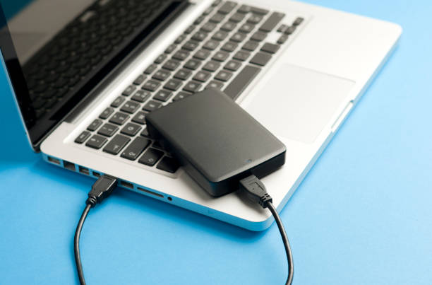 istock black external hard drive with cable (usb), above laptop, blue table. 1204299363