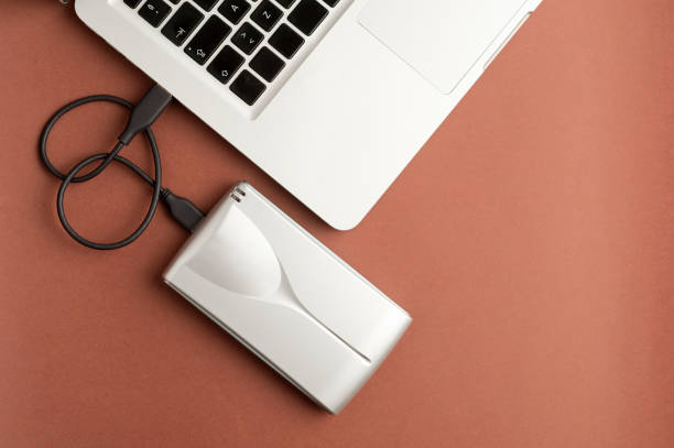 istock Aluminum external hard drive with cable (usb) connected to laptop, on brown office table.Top view 1204299430