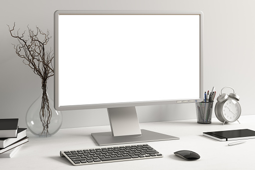 Workspace with blank computer monitor white screen mock up on the white desk near white wall.