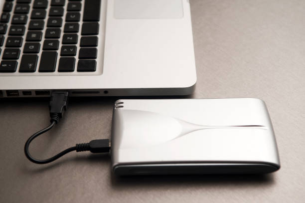 istock silver external hard drive, partial laptop view, on aluminum table 1204299504