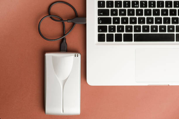 istock Aluminum external hard drive with cable (usb) connected to laptop, on brown office table.Top view 1204299526