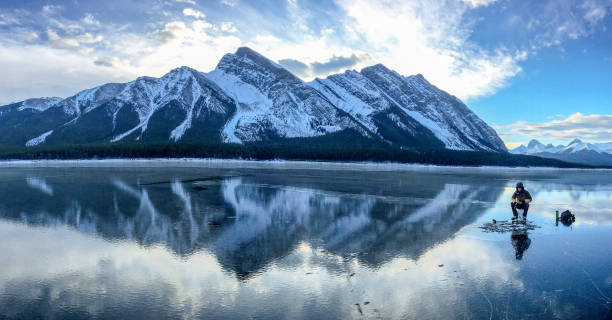 Ice fishing on frozen mountain lake Ice fisherman waits for a catch in beautiful mountain landscape man ice fishing stock pictures, royalty-free photos & images